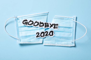 Metin Elveda 2020 Ve açık mavi arka planda tıbbi yüz maskesi, düz yatıyordu