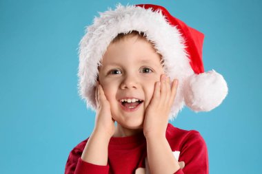 Açık mavi arka planda Noel Baba şapkalı şirin çocuk. Noel kutlaması