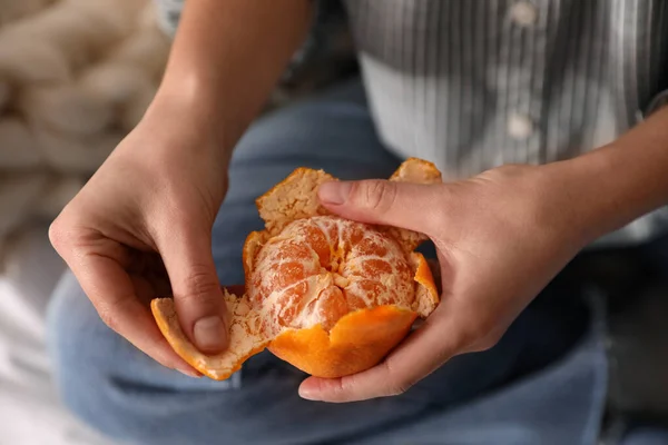 Woman peeling fresh tangerine on blurred background, closeup