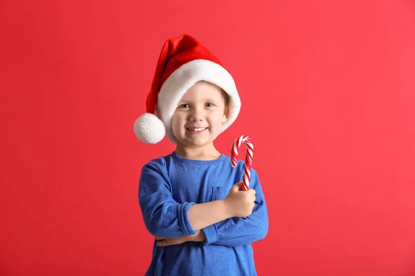 Симпатичный Маленький Мальчик Шляпе Санта Клауса Держит Конфетку Красном Фоне — стоковое фото