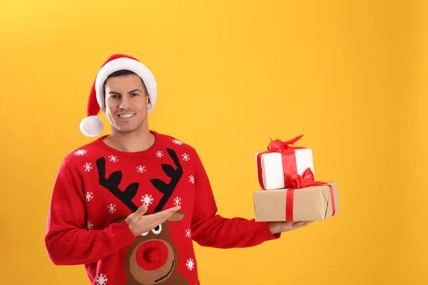 Schöner Mann Mit Weihnachtsmütze Hält Geschenkboxen Auf Gelbem Hintergrund — Stockfoto