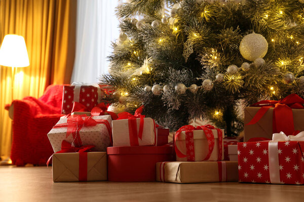 Pile of gift boxes near beautiful Christmas tree indoors