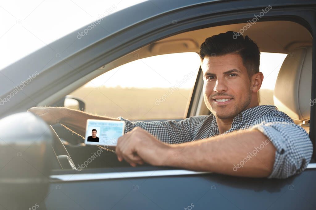Happy man holding license while sitting in car outdoors. Driving school