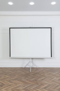 Beyaz duvarın yanındaki boş projeksiyon ekranı. Tasarım için boşluk