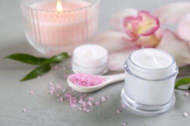Kozmetik ürünleri, çiçekler ve açık gri masadaki mumlarla güzel bir spa kompozisyonu. Metin için boşluk