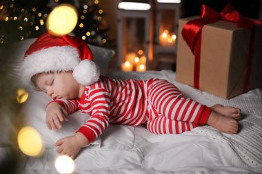 Noel pijamalı bebek ve Noel Baba şapkalı bebek kapalı bir odada hediye kutusunun yanında uyuyor.