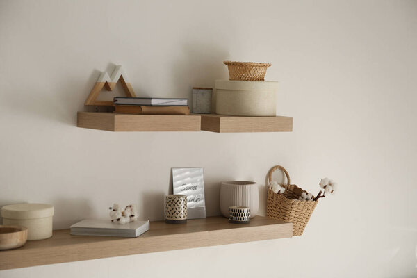 Wooden shelves with books and different decorative elements on light wall