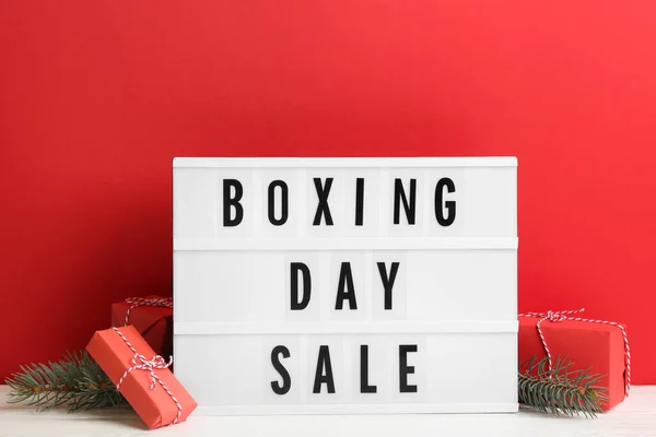Composition with Boxing Day Sale sign and Christmas gifts on white table against red background