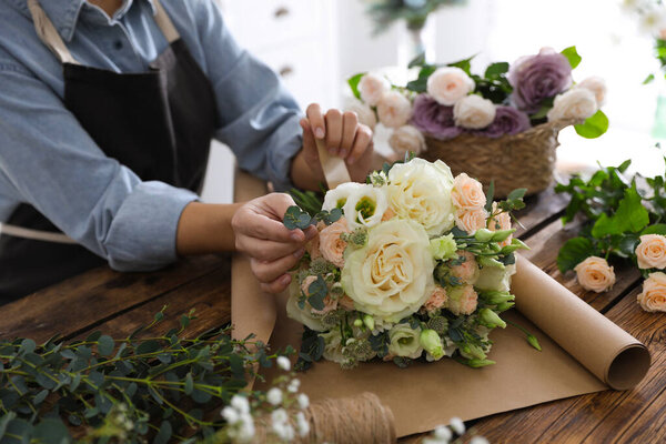 Florist making beautiful wedding bouquet at wooden table, closeup