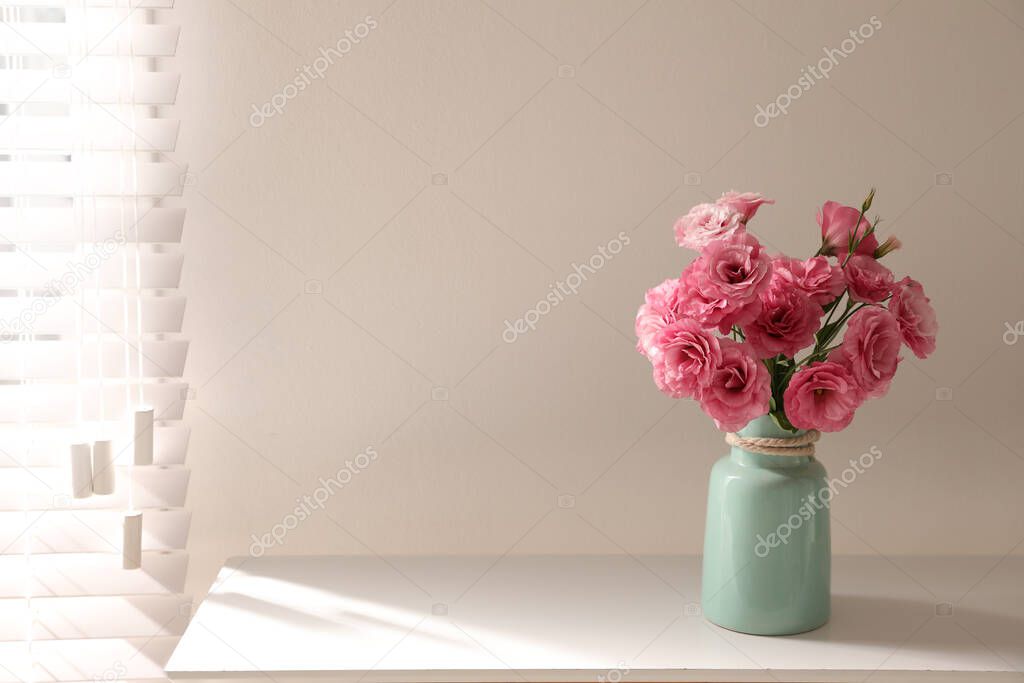 Bouquet of beautiful Eustoma flowers on table near light wall. Space for text
