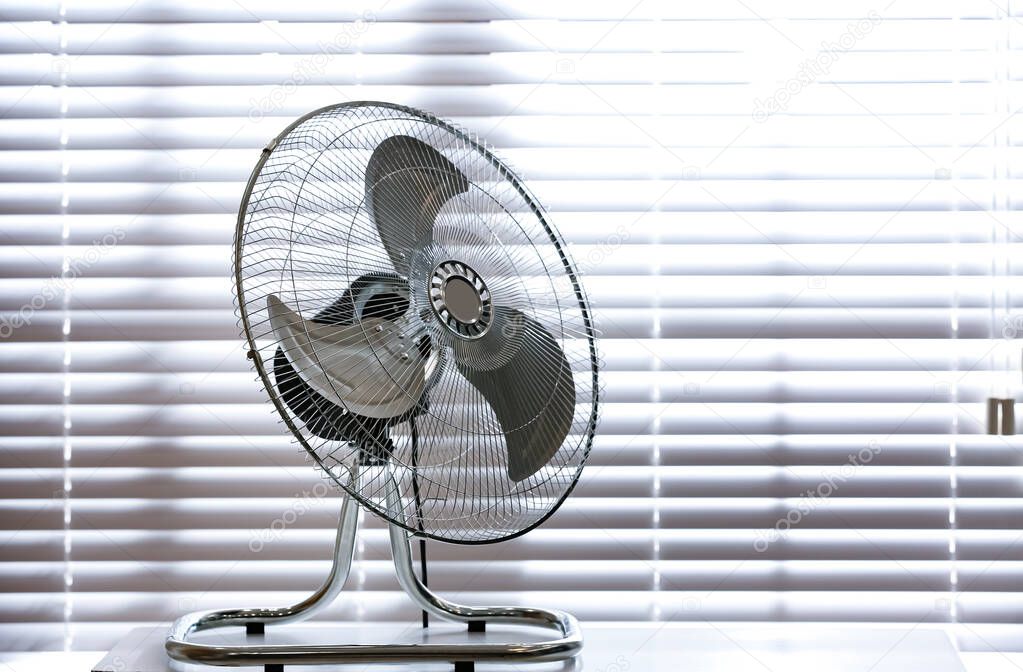 Modern electric fan on table near window indoors. Space for text