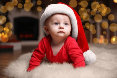 Kırmızı pijamalı şirin bir bebek ve yerde bulanık ışık karşısında Noel Baba şapkası. Noel elbisesi
