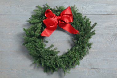 Noel çelengi, gri ahşap arka planda kırmızı fiyonklu köknar dallarından yapılmıştır.