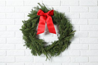 Beyaz tuğla duvarda kırmızı fiyonklu köknar dallarından yapılmış Noel çelengi.