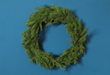 Mavi duvardaki köknar dallarından yapılmış Noel çelengi