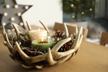 Yanan kokulu kozalaklı mumlar, içinde Noel dekoru olan ahşap masa.