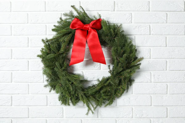 Beyaz tuğla duvarda kırmızı fiyonklu köknar dallarından yapılmış Noel çelengi.