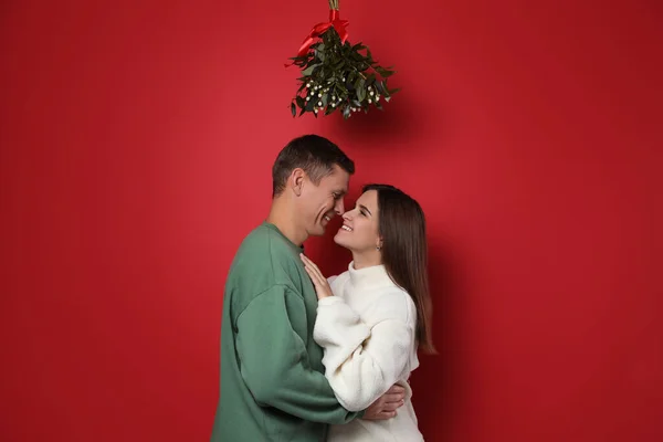 Feliz Pareja Pie Bajo Manojo Muérdago Sobre Fondo Rojo —  Fotos de Stock