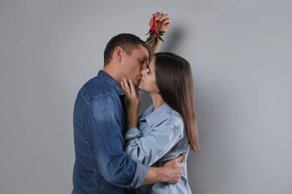 Happy Couple Kissing Mistletoe Bunch Grey Background — Stock Photo, Image