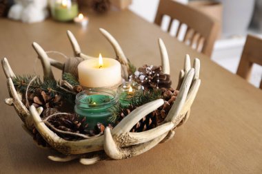 Yanan kokulu kozalaklı mumlar, içinde Noel dekoru olan ahşap masa.