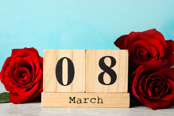 木製のブロックカレンダー3月8日の日付とライトブルーの背景にテーブルの上にバラ 国際女性デー — ストック写真