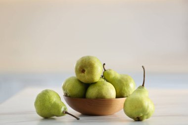 Beyaz masada taze olgun armutlarla dolu bir kase.