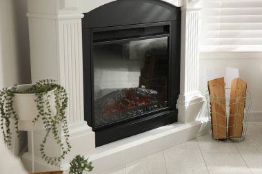 Parlak oturma odasının içinde yapay şömine ve sepetin içinde odun var.