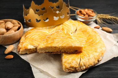 Geleneksel galette des Rois, siyah ahşap masa üzerinde kağıt taç, yakın plan.
