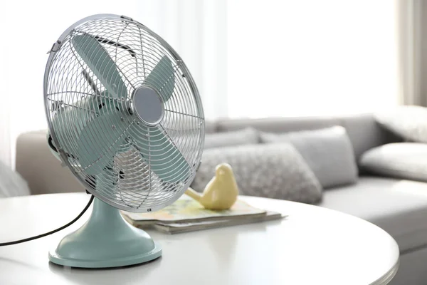 Modern electric fan on table in living room, space for text. Summer heat