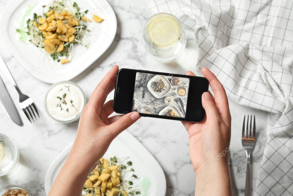 Blogger taking photo of salad at marble table, top view