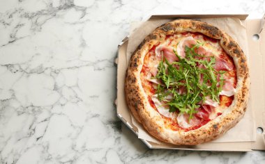 Lezzetli pizza et ve roka karton kutuda beyaz mermer masa, üst manzara