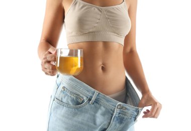 Yaşlı, büyük kotlu ve elinde çay bardağı olan genç bir kadın beyaz arka planda diyet sonuçlarını gösteriyor.