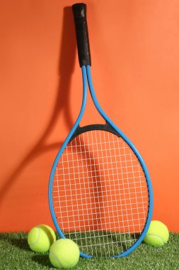 Tenis raketi ve toplar yeşil çimlerin üzerinde turuncu arka plana karşı. Spor malzemeleri.