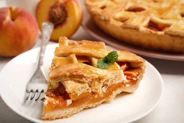 Piece of delicious fresh peach pie served on white table, closeup