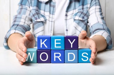 Beyaz masada KEYWORDS sözcüğüyle renkli küpleri sergileyen kadın, yakın plan
