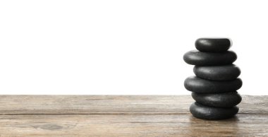 Beyaz arka plana karşı ahşap masadaki spa taşları yığını. Metin için boşluk