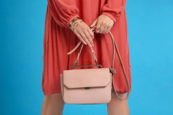 Young woman with stylish pink bag on light blue background, closeup