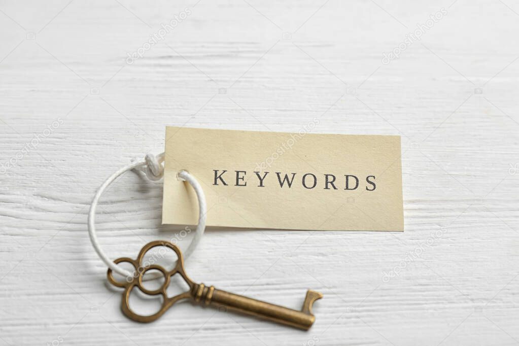 Key with tag KEYWORDS on white wooden background