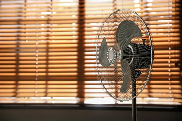 Modern electric fan near window indoors. Space for text