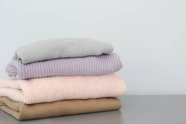 Stack of folded warm knitted sweaters on grey table