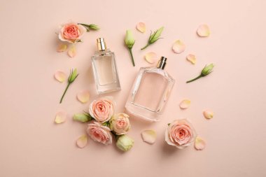 Flat lay composition with different perfume bottles and fresh flowers on beige background clipart