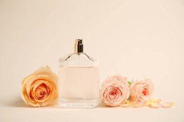 Bej arka planda güller olan bir şişe parfüm.