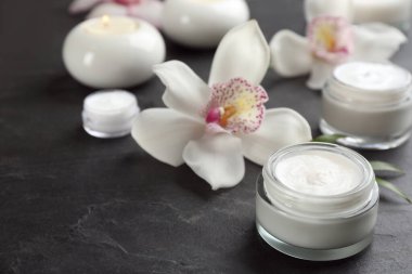 Siyah masa üzerinde kozmetik ürünleri ve çiçekleri olan güzel bir spa kompozisyonu, yakın plan. Metin için boşluk