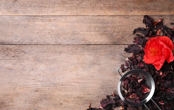 Dry hibiscus tea, sieve and flower on wooden table, flat lay. Space for text