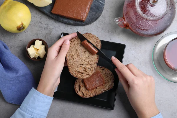 女人在灰色桌子上的吐司面包上涂上美味的昆斯酱 — 图库照片