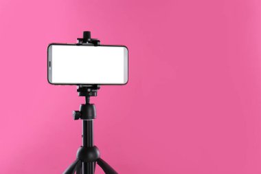 Beyaz ekranlı akıllı telefon pembe arka planda tripoda sabitlendi. Metin için boşluk