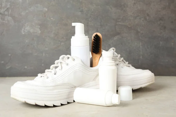 Composition with stylish footwear and shoe care accessories on white table against grey background