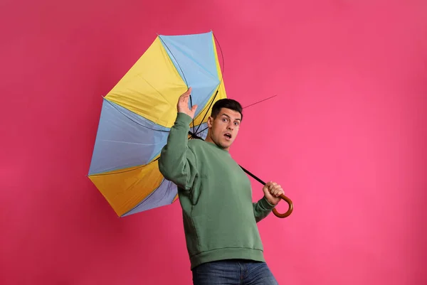 情绪激动的男人 带着雨伞 带着粉红的背景 被大风吹得落花流水 — 图库照片