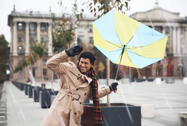 Man with colorful umbrella caught in gust of wind on street