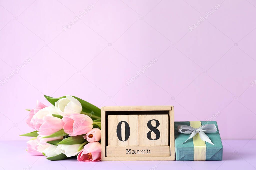 Wooden block calendar with date 8th of March, tulips and gift box on lilac background, space for text. International Women's Day
